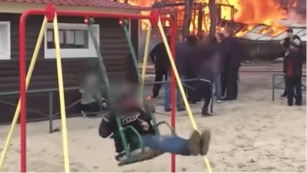 Niño. Niño juega mientras una casa se incendia a sus espaldas.